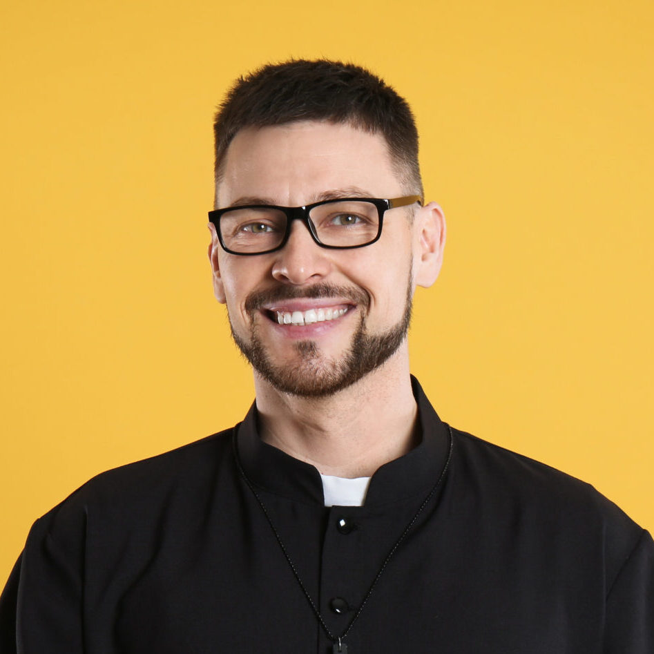 Priest,In,Cassock,With,Bible,On,Yellow,Background